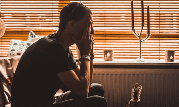 Man on couch by window, reflecting on reasons